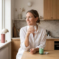 Spirulina & Chlorella Noop – livsstilsbild, kvinna i köket med glas vatten och förpackningen